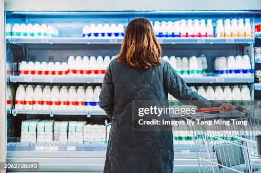 Rear view shot of a female customer looking and choosing fresh bottled milk while standing in front of a display fridge full of diary products in supermarket. The concept of choice. Rear view shot of a female customer looking and choosing fresh bottled milk while standing in front of a display fridge full of diary products in supermarket. The concept of choice.