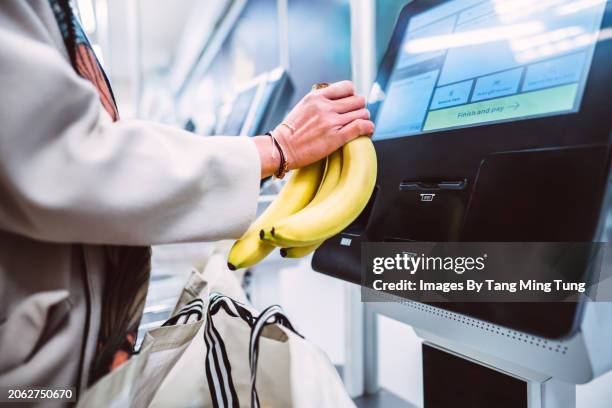 a woman scanning a bunch of bananas at the self checkout in supermarket - grocery check out lane fotografías e imágenes de stock