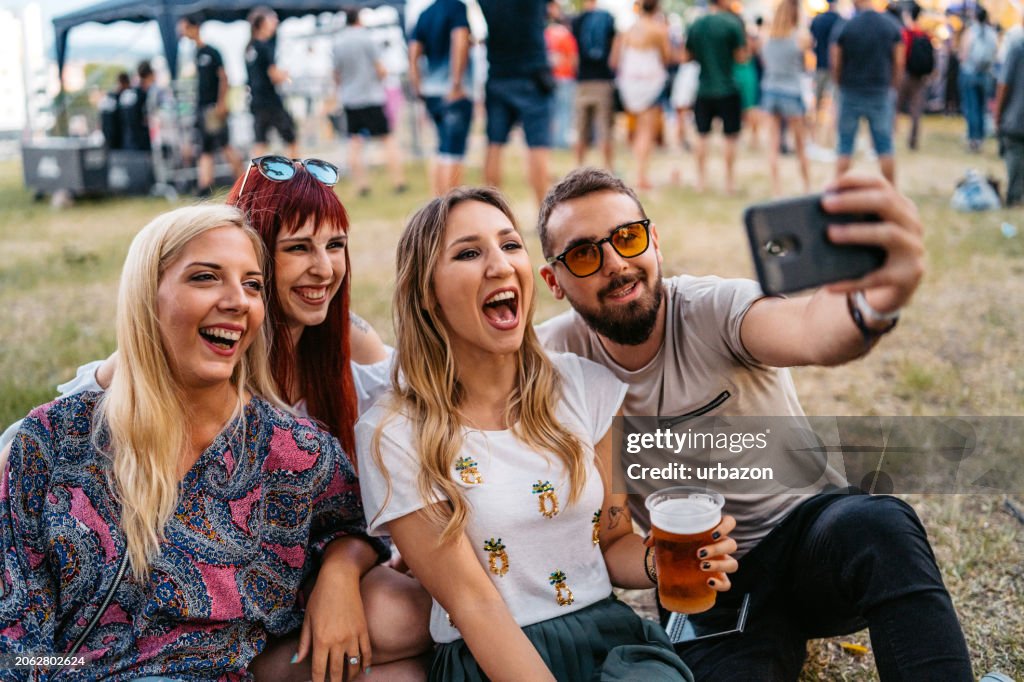 Group Of People Sitting On A Grass And Taking Selfies At The Music Festival