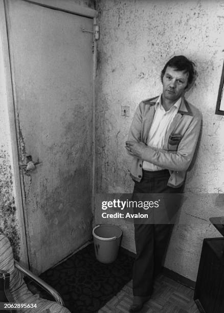 Man stands in a property with moldy walls, London, 1981.