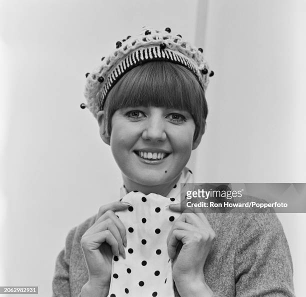 English singer Cilla Black posed tying a white scarf with black polka dots in London circa 1966.