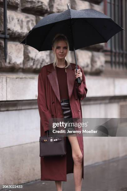 Leonie Hanne seen wearing a dark red long trenchcoat, red shirt, black leather skirt, belt, Hermes Birkin handbag outside Hermes show, during the...