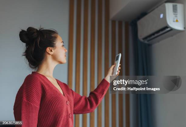 heat pump in air conditioning system. woman adjusting temperature, holding remote controller. using heat pump for heating, cooling in modern house. environmentally friendly and sustainable solution for smart home. - airconditioning stockfoto's en -beelden