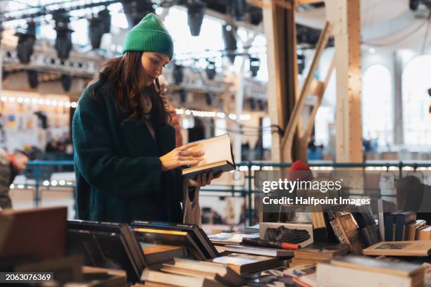 beautiful woman shopping used books in thrift store, second-hand bookstore. generation z student shopping at flea market. concept of recycling, upcycling and environmental sustainability. - librería fotografías e imágenes de stock