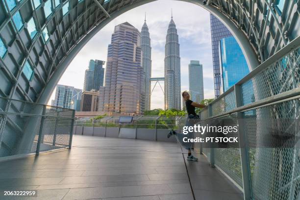 a woman stands at the tunnel saloma overlooking the petronas twin towers. - town stock illustrations bildbanksfoton och bilder