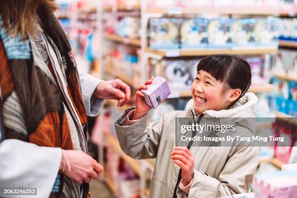 lovely cheerful girl shopping for toys with her mom in toy shop joyfully - woman picking up toys stock pictures, royalty-free photos & images