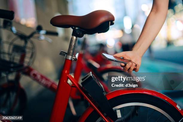 cropped shot of woman's hand holding smartphone using rental bike app to scan the qr code. renting bicycle from bike-sharing services in the city. shared transport service. sustainable living concept - sharing economy stock-fotos und bilder