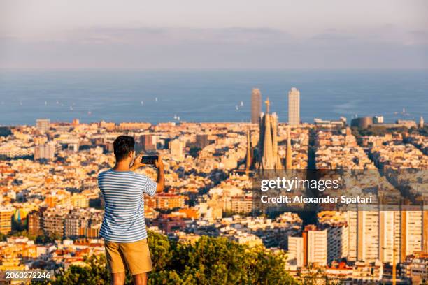 man taking photo of barcelona skyline with sagrada familia at sunset, spain - barcelona day photos et images de collection