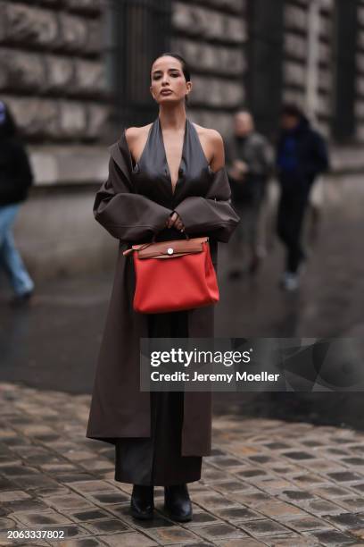 Fashion Week Guest seen wearing a silk grey v-top, long black leather dress, brown leather coat, black boots and a red Hermes Herbag outside Hermes...