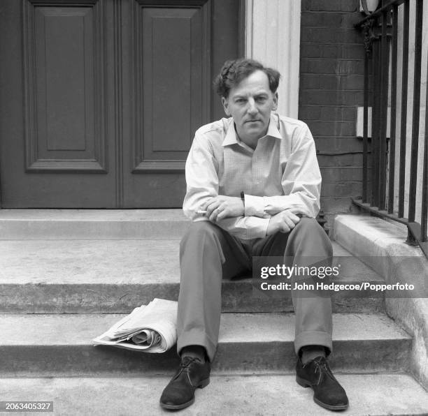 English novelist, journalist and writer Keith Waterhouse seated with a bundle of newspapers and magazines on the front steps of his house in London...