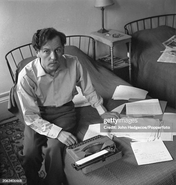 English novelist, journalist and writer Keith Waterhouse seated on a bed with papers and a typewriter inside his house in London in 1959.
