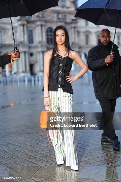 Mitsuki Kimura wears a black off-shoulder corset / top, a striped pants , an orange / brown leather bag, pointed shoes, outside Louis Vuitton, during...