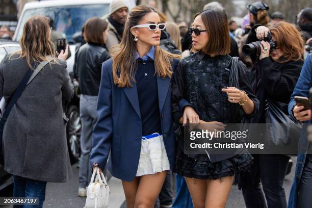 Camila Coelho wears white mini skirt, navy blue blazer, white bag, sunglasses & Aimee Song wears black skirt, bag, shirt outside Miu Miu during the...