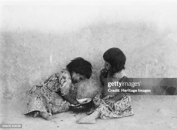 Moki melon eaters, circa 1900. Two Hopi girls seated on ground eating melons. Creator: Edward Sheriff Curtis.