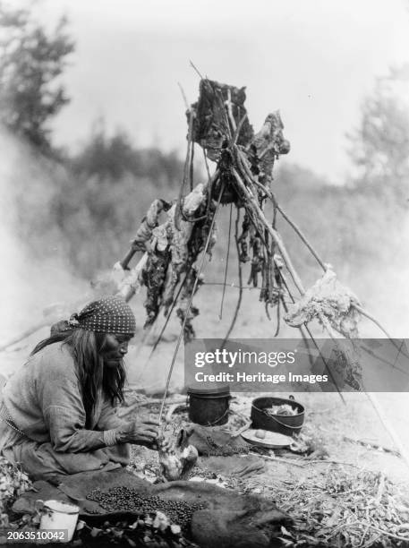 Sarsi kitchen, circa 1927. Sarsi woman cooking over campfire, Alberta, Canada. Creator: Edward Sheriff Curtis.