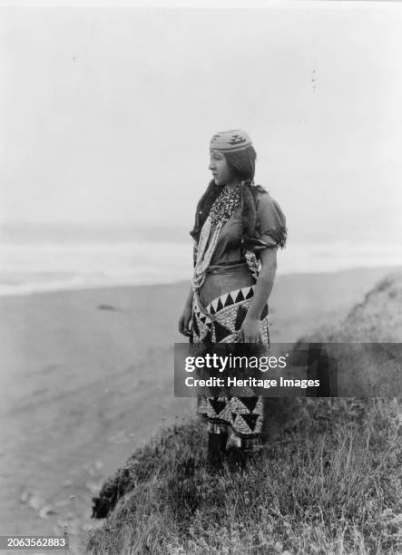Woman's primitive dress-Tolowa, circa 1923. Ada Lopez Richards, full-length portrait, standing near the shore wearing hat, necklaces, and dress....