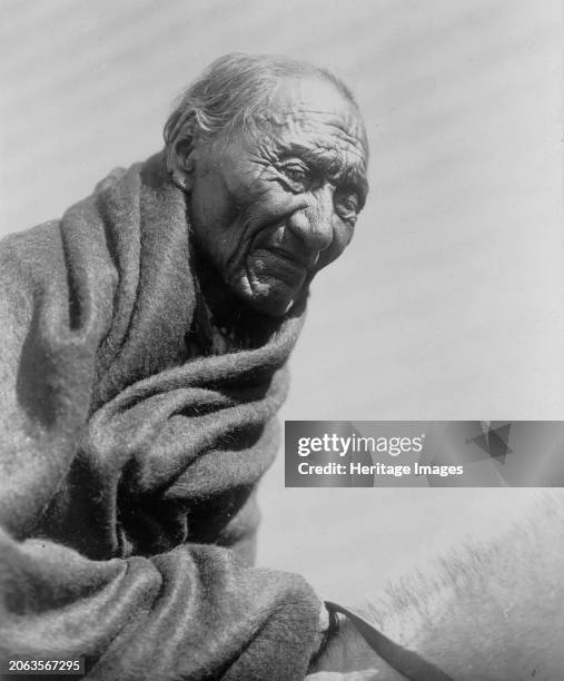 Morning Eagle, circa 1910. Elderly Piegan man, half-length portrait, wrapped in blanket, seated on horse, facing front. Creator: Edward Sheriff...