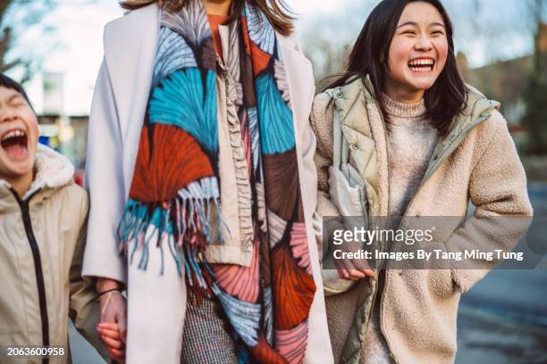 laughing daughters having fun with their mom while walking in high street of town - thier stock pictures, royalty-free photos & images