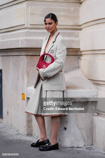 Guest wears a ww oversized blazer jacket, a red leather bag, a knee-length skirt , black leather flat loafers shoes, outside Miu Miu , during the...