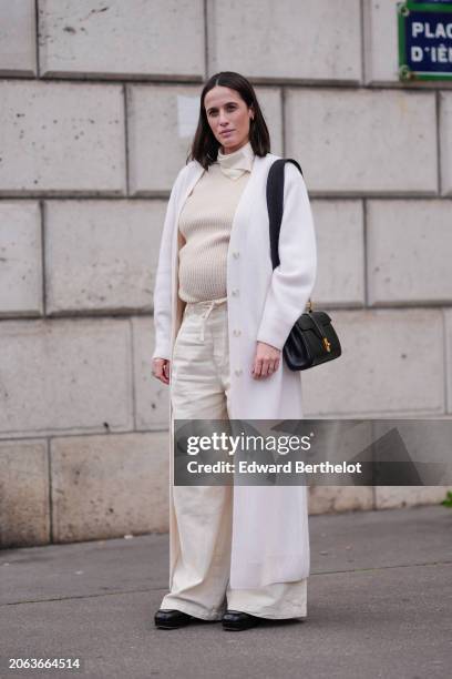 Astrid Boutrot wears a white turtleneck ribbed wool pullover , a white long coat , a bb leather bag, white wide-leg denim flared pants , leather...