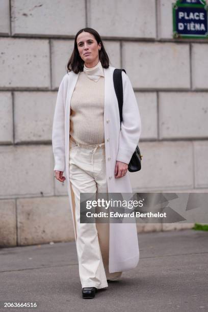 Astrid Boutrot wears a white turtleneck ribbed wool pullover , a white long coat , a bb leather bag, white wide-leg denim flared pants , leather...