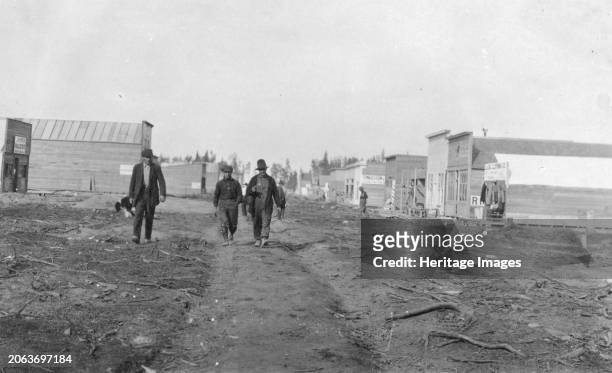 Three men walking down a dirt road, through town, between circa 1900 and 1916. Creator: Unknown.