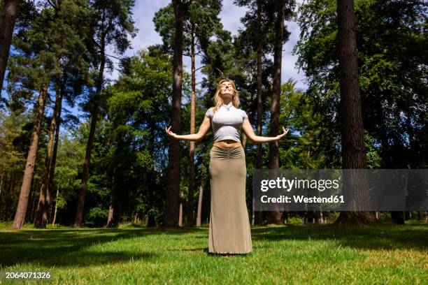 smiling young woman standing with arms raised in front of trees on sunny day - green skirt stock pictures, royalty-free photos & images