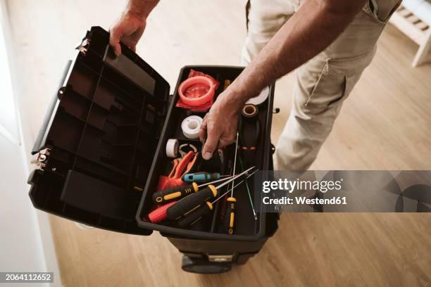 mature technician picking up tools from box at home - gereedschap stockfoto's en -beelden