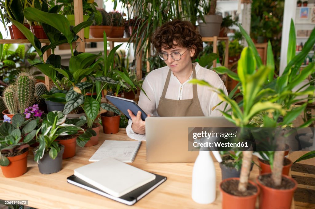 Botanist with laptop and tablet PC at table in plant shop