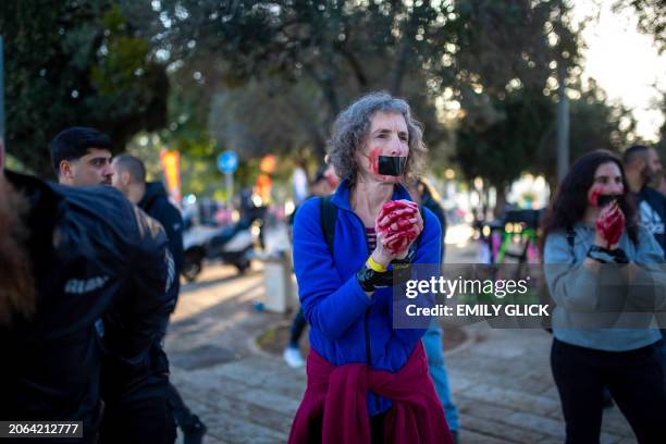 Woman stands with her hands duct taped together, duct tape over her mouth, and her hands dyed the color of blood, as she protests for the return of...