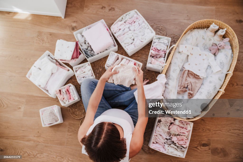 Expecting pregnant woman arranging baby clothes near moses basket at home