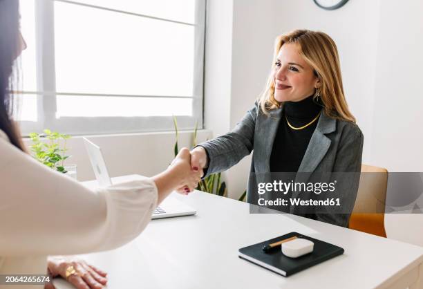 smiling hr manager shaking hands with candidate at desk - colloquio di lavoro foto e immagini stock