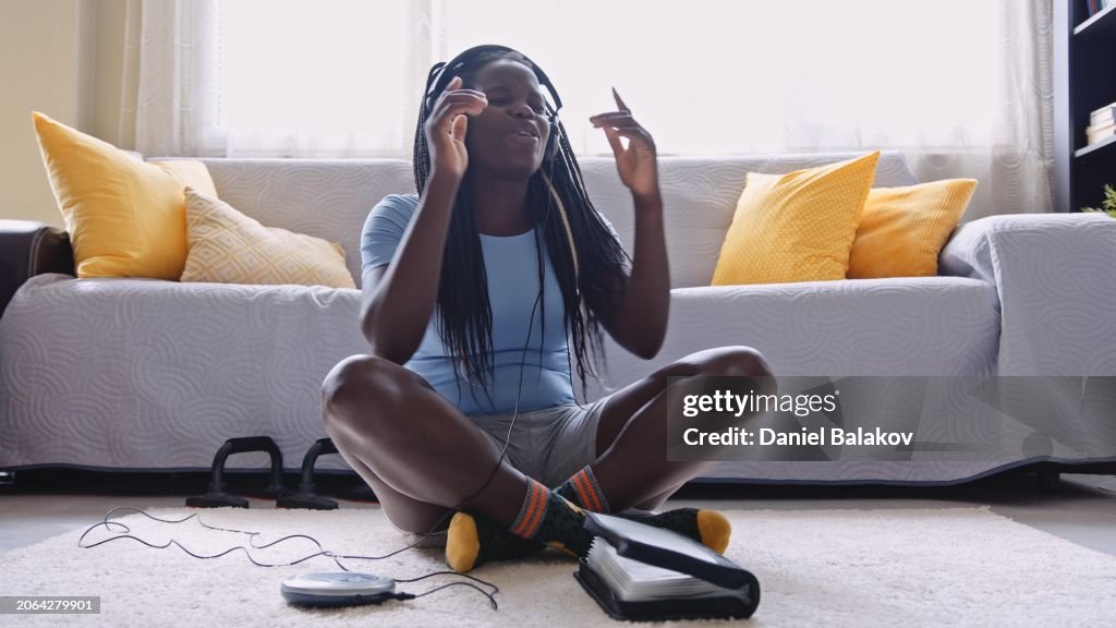Black girl listens to music on portable CD player at home. Music therapy.
