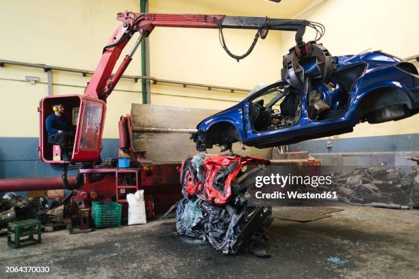 mechanic operating crane machine and carrying scrapped car at workshop - car crushing machine stock pictures, royalty-free photos & images