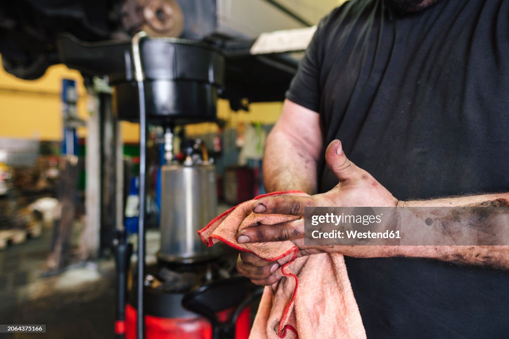 Mechanic cleaning hands with rag at workshop