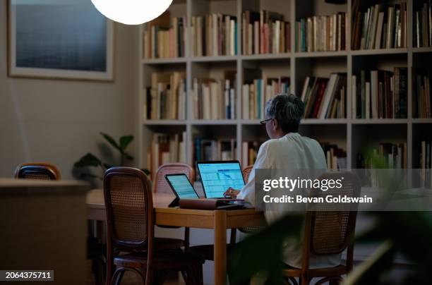 laptop, investment and retirement with senior woman in dining room of home at night for accounting or budget. computer, savings or finance and elderly pensioner person in apartment with bank invoice - eetkamer stockfoto's en -beelden