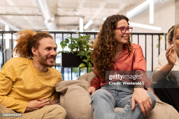 businesswoman with curly hair sitting amidst colleagues at co-working space - sitzsack stock-fotos und bilder