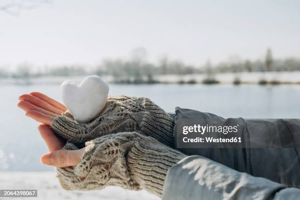 hands of woman holding heart shaped snowball near lake - fingerless glove stock pictures, royalty-free photos & images