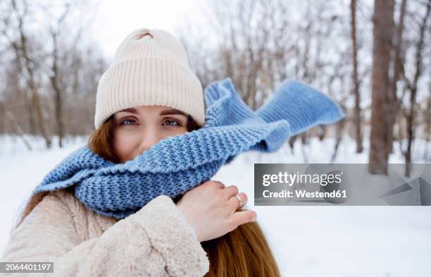 young woman wearing knit hat and blue scarf in winter forest - woman flying scarf stock pictures, royalty-free photos & images