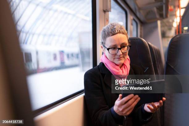 mature businesswoman using tablet pc near window in train - older woman colored hair stock pictures, royalty-free photos & images