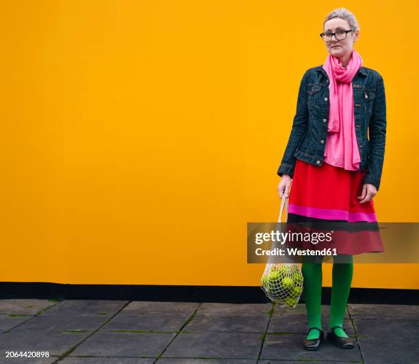 mature woman carrying groceries in front of yellow wall - vibrant stock pictures, royalty-free photos & images