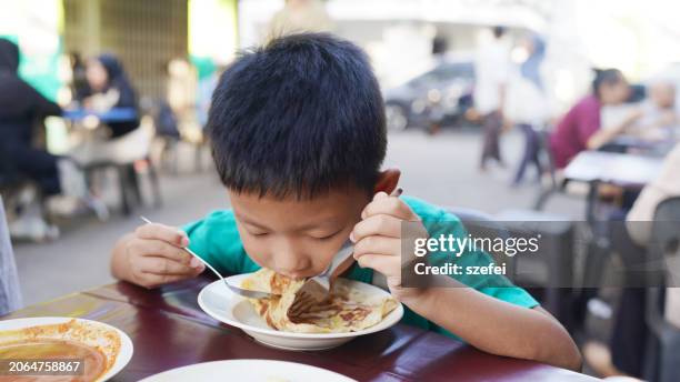 young asian boy eating indian street food roti canai, penang island, malaysia - roti canai stock pictures, royalty-free photos & images