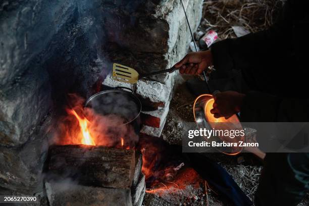 Migrant cooks in a corner and uses the fire to warm himself during the winter inside the Silo, a crumbling building lacking sanitation, drinking...