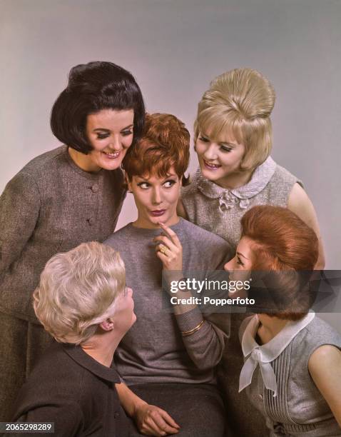 Posed studio portrait of five female fashion models dressed in a range of light grey neutral coloured outfits, they stand close together to admire...