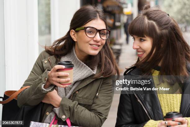 women chatting, while walking on city street. - coffee to go cups stock pictures, royalty-free photos & images