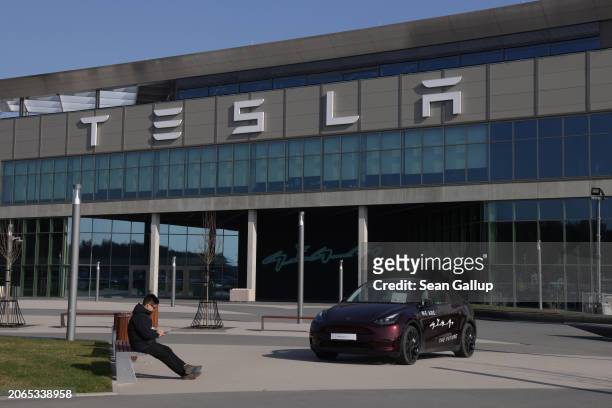 Man sits at the entrance to the Tesla Gigafactory on March 07, 2024 near Gruenheide, Germany. Tesla has announced that it is suspending production at...