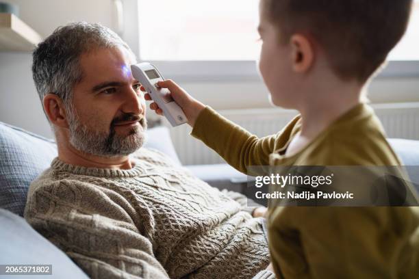 son taking dad's temperature using a digital thermometer - infrared thermometer stock pictures, royalty-free photos & images