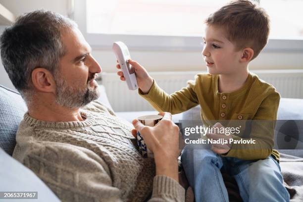 son taking dad's temperature using a digital thermometer - infrared thermometer stock pictures, royalty-free photos & images