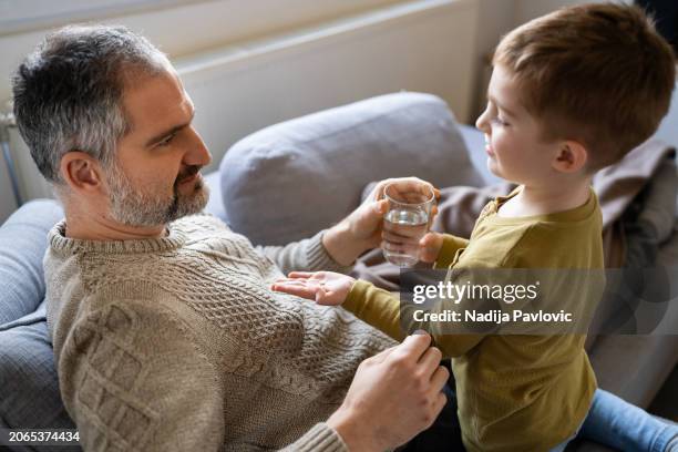 hijo cuidando a su padre enfermo - niño-tomando-agua fotografías e imágenes de stock