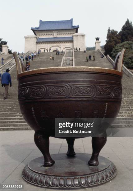 Bronze ding, an ancient Chinese vessel symbolizing power, pictured with the main hall of the Sun Yat-sen Mausoleum in the background, Nanjing, China,...